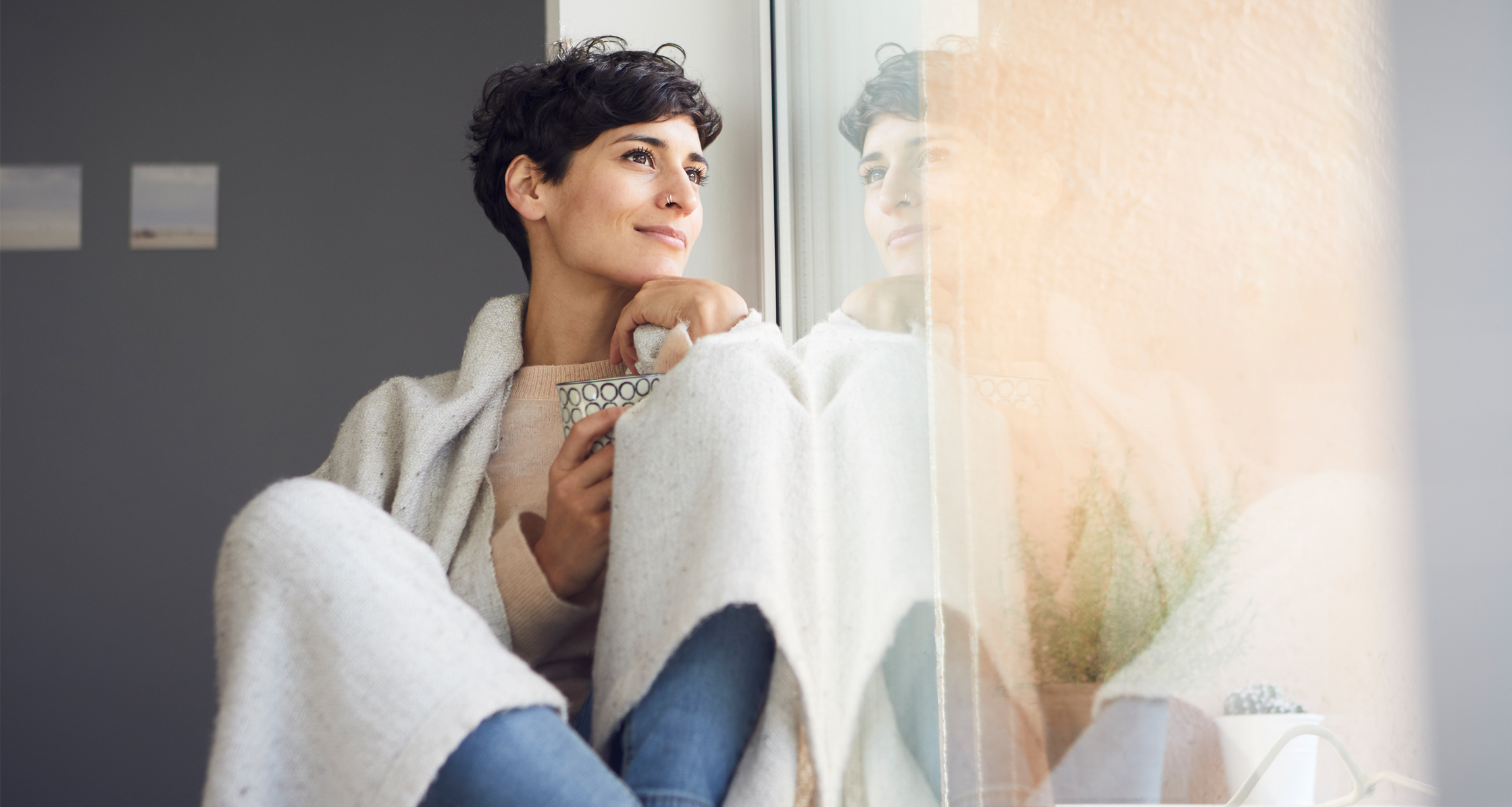 Woman recharging at home sitting at the window holding cup of tea