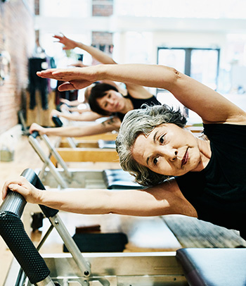 Senior woman doing Pilates on reformer during class in a studio.