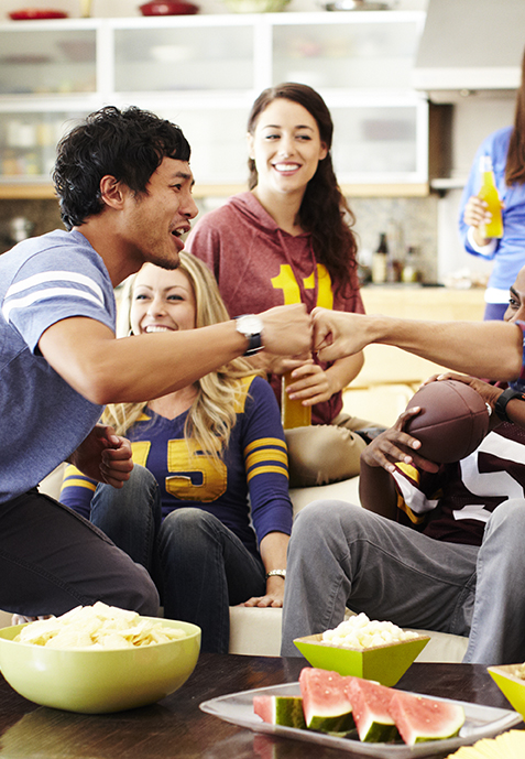 Friends fist bumping while watching a football game mid-day in living room.