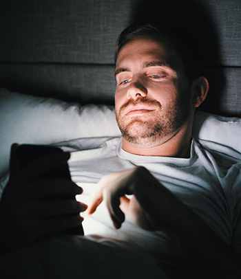 Man in bed looking at his phone.