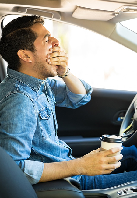Young man feeling tired and yawning while driving a car.