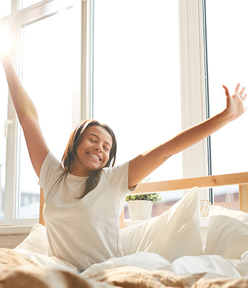 Woman stretching sitting in bed lit by sunlight.