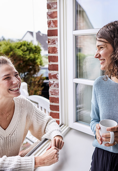 Two happy women talking through the window.