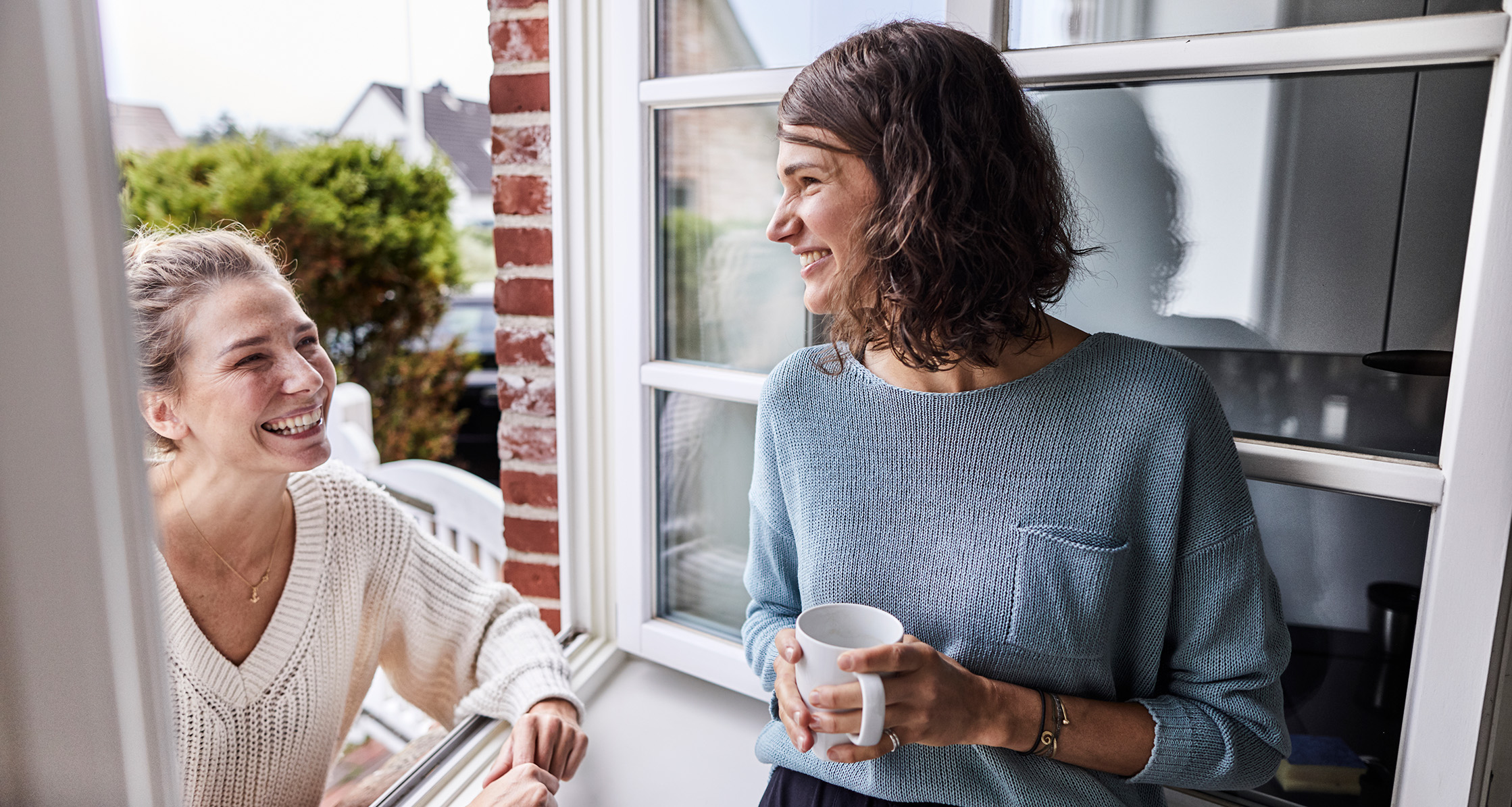 Two happy women talking through the window.