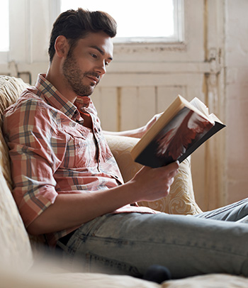 Man sitting on sofa reading a book.