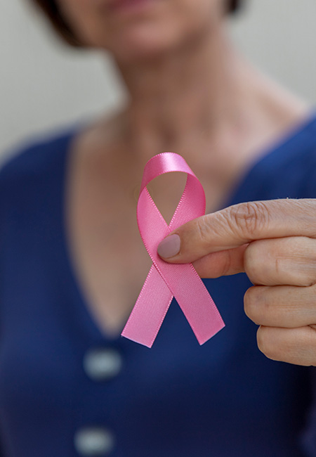 Woman holding a pink bow in her hand for breast cancer prevention.