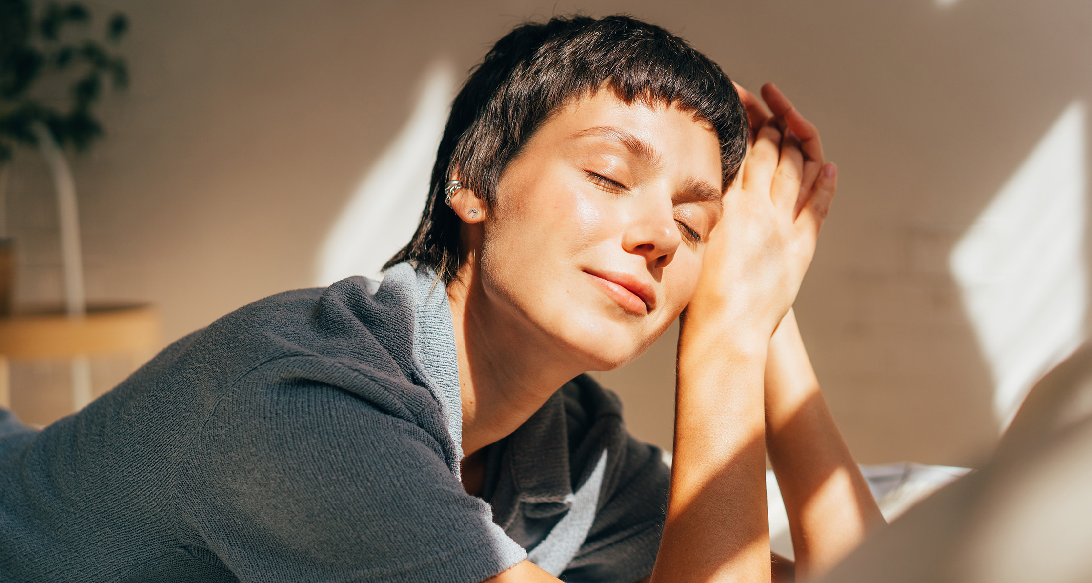 A woman lies on a bed in bright sunlight from the window.