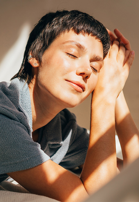 A woman lies on a bed in bright sunlight from the window.