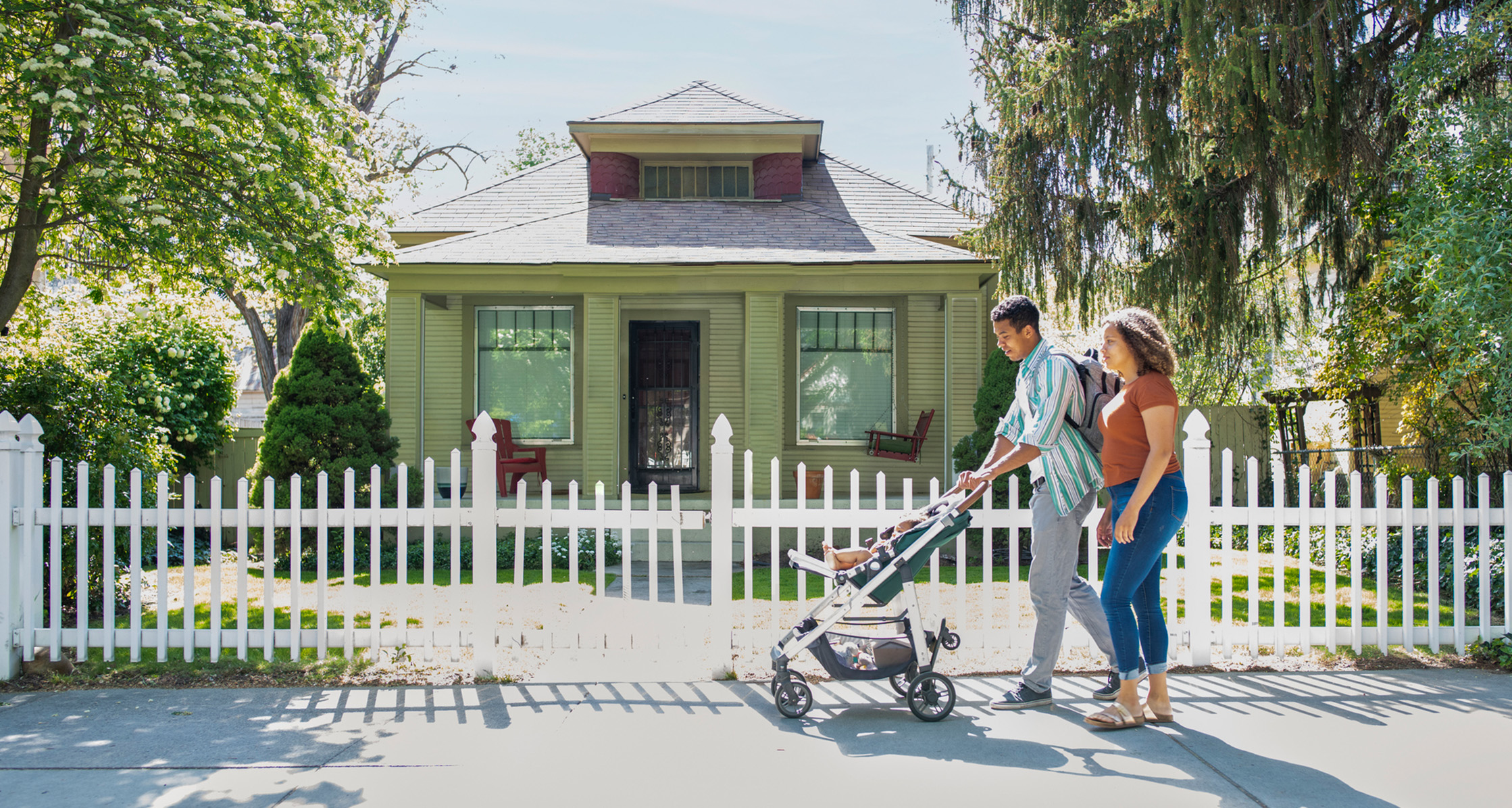 Mother and father walking with baby in stroller on neighborhood sidewalk.