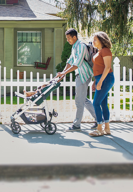 Mother and father walking with baby in stroller on neighborhood sidewalk.