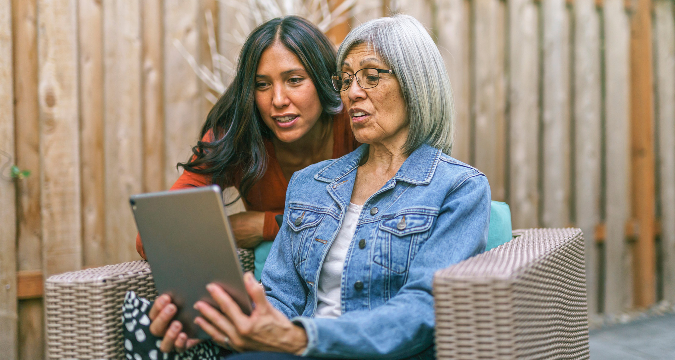 A woman and her elderly mother use a tablet together to discuss their family health history.