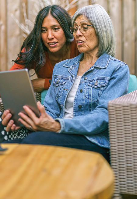 A woman and her elderly mother use a tablet together to discuss their family health history.