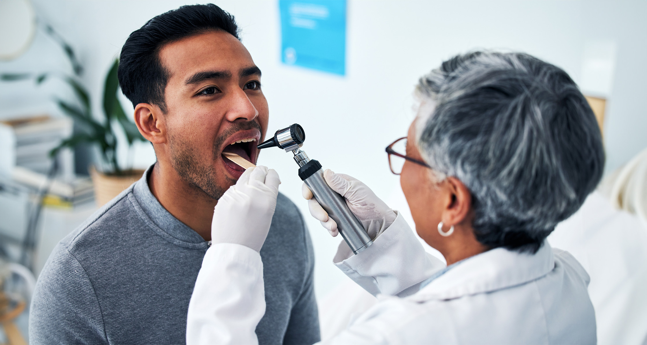 A health care provider consults with a man in a hospital and examines his throat.