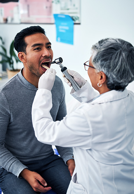 A health care provider consults with a man in a hospital and examines his throat.