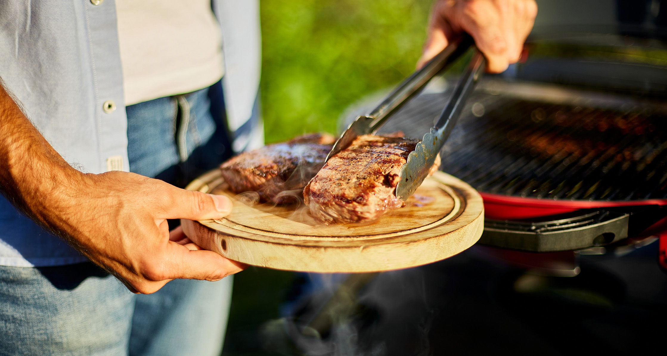 A man taking steaks off the grill.