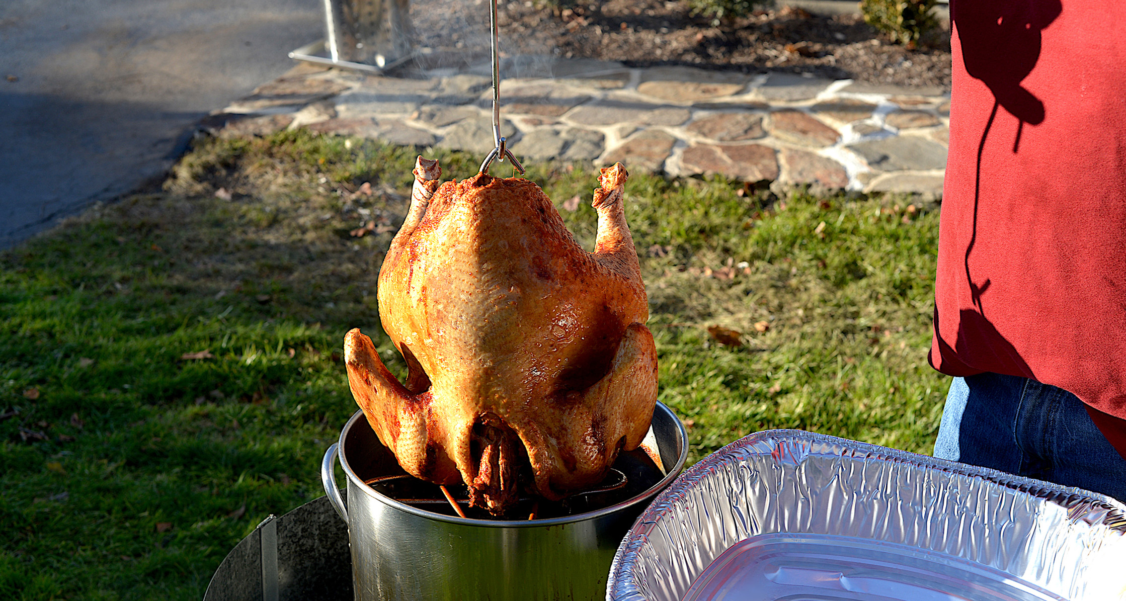 Ensuring safety, an individual carefully removes a fried turkey from the fryer outdoors.