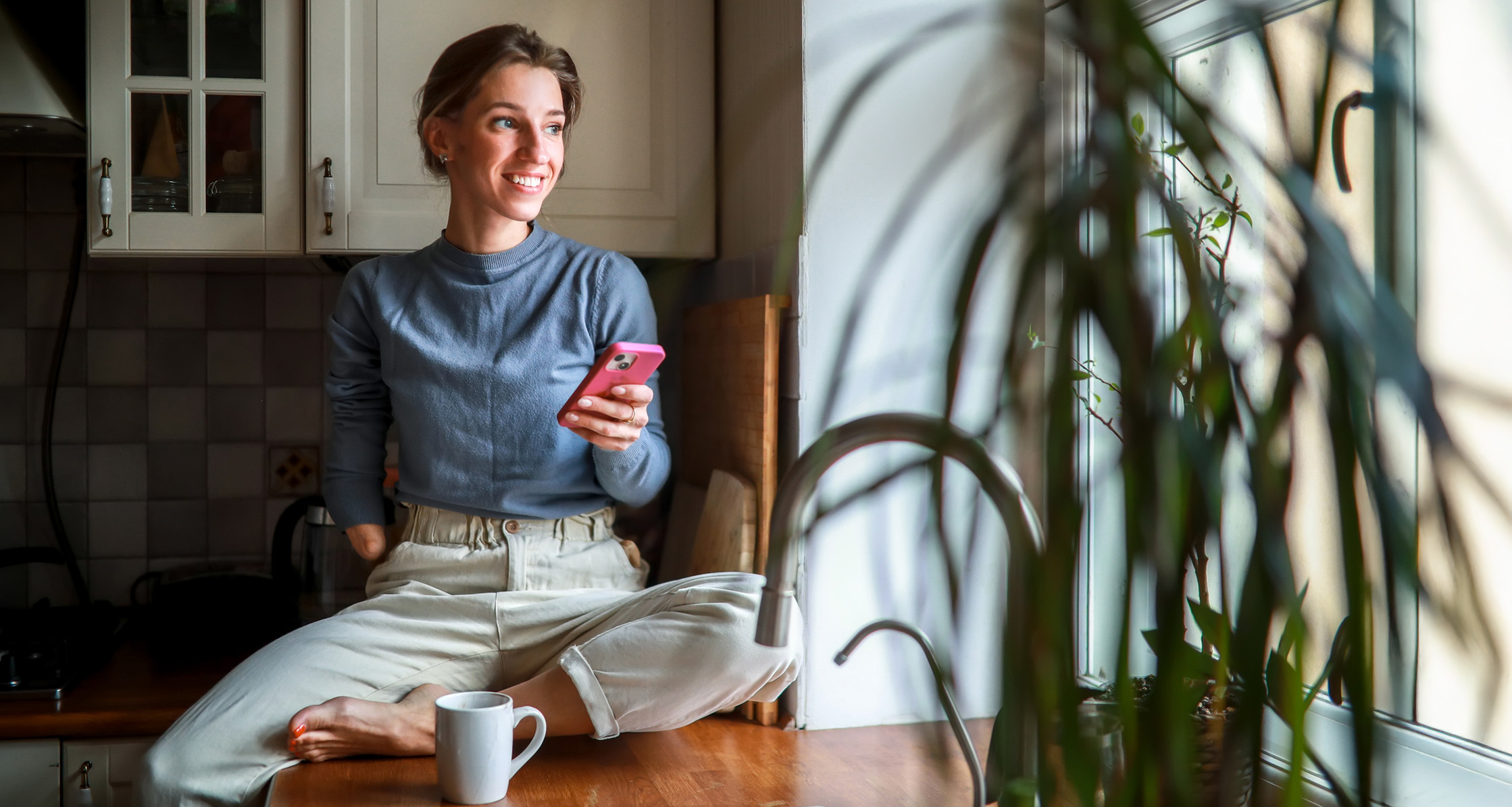 A disabled Veteran sits on a counter, legs crossed, reviewing her accomplishments on the phone.