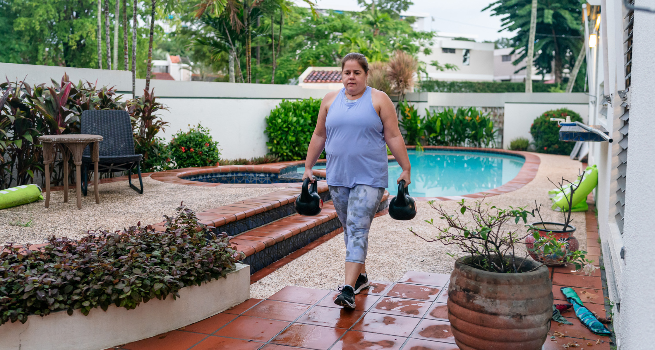 A person is exercising with kettlebells in her backyard, showcasing functional fitness.