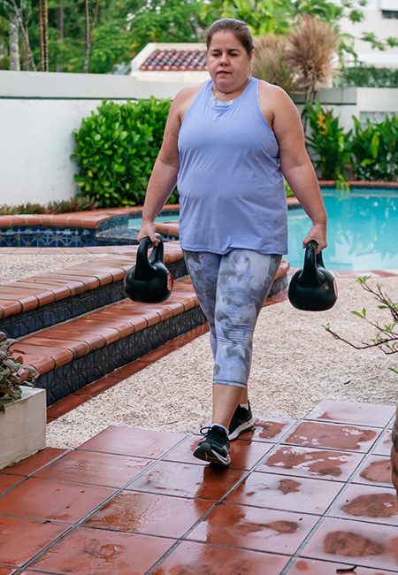 A person is exercising with kettlebells in her backyard, showcasing functional fitness.