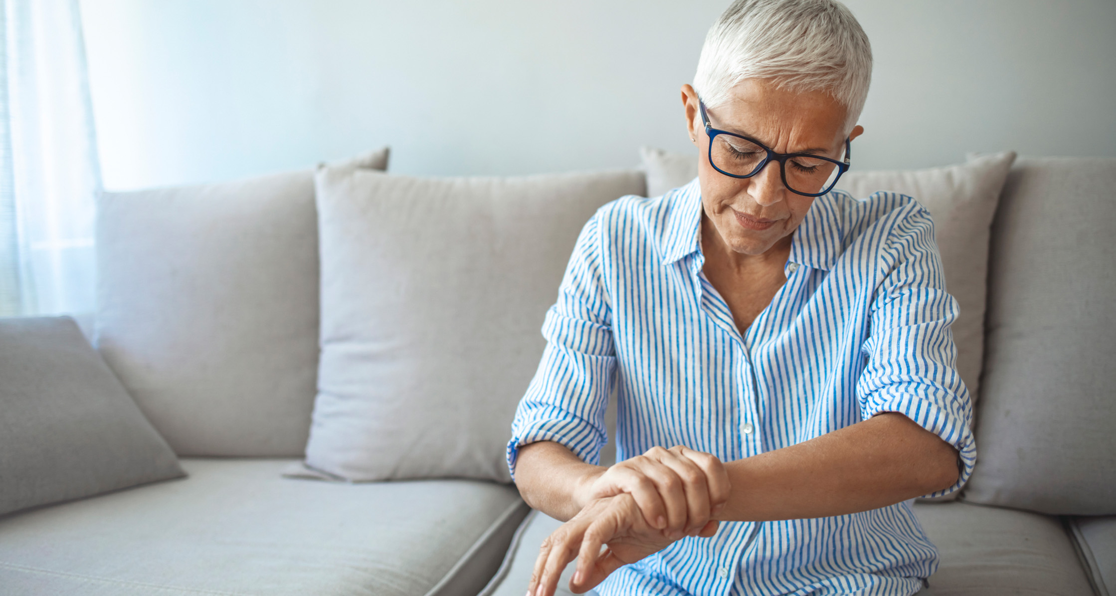 A woman is sitting on a couch, suffering from chronic inflammation and pain in her wrist joints.