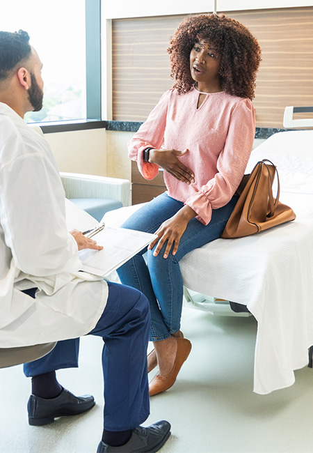 A woman sitting on a bed talking to a doctor about stomach pain.