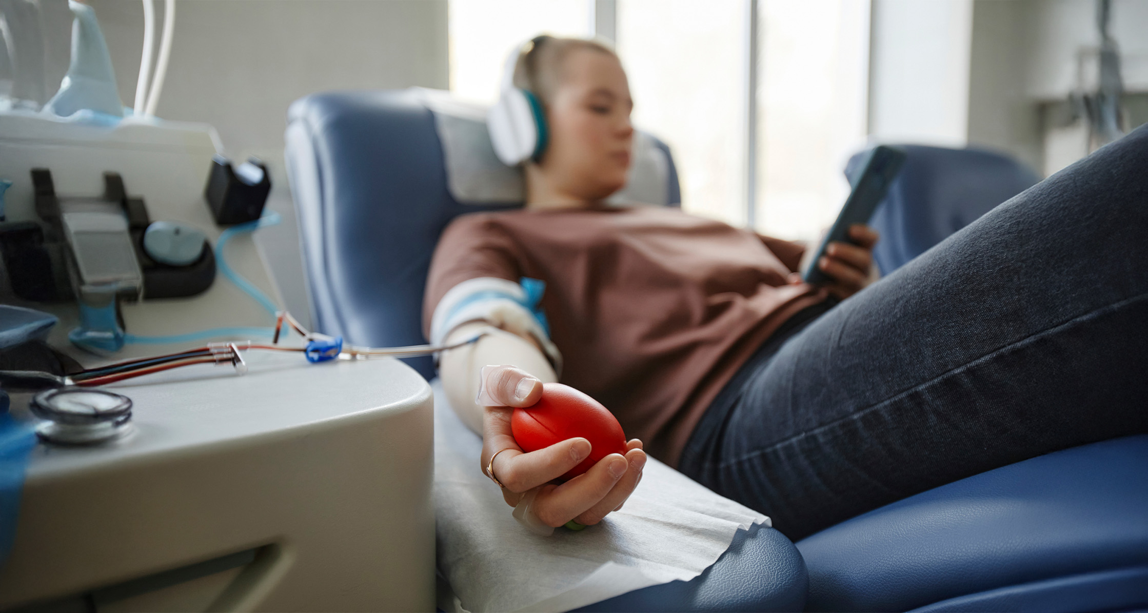 A woman's hand is shown holding a softball while lying on a couch at a blood donation center.