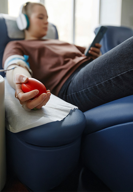 A woman's hand is shown holding a softball while lying on a couch at a blood donation center.