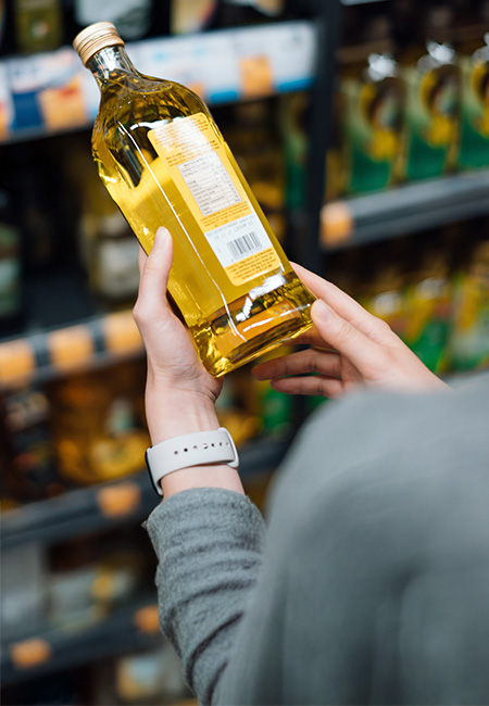 Close-up of a person in a grocery store holding a bottle of cooking oil and reading the nutritional label.