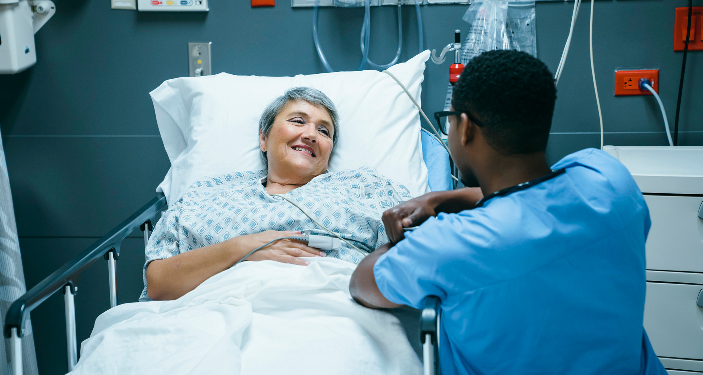 A nurse talking to a patient after surgery in a hospital bed.