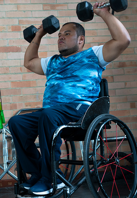 A Veteran in a wheelchair is exercising with dumbbells at a gym, showcasing accessible fitness.