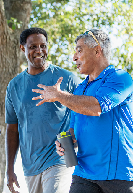 A group of male Veterans are exercising outdoors in a sunny park, taking a break to chat and drink water.