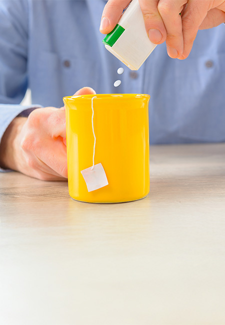 Close-up of a person using saccharin pills in hot tea.