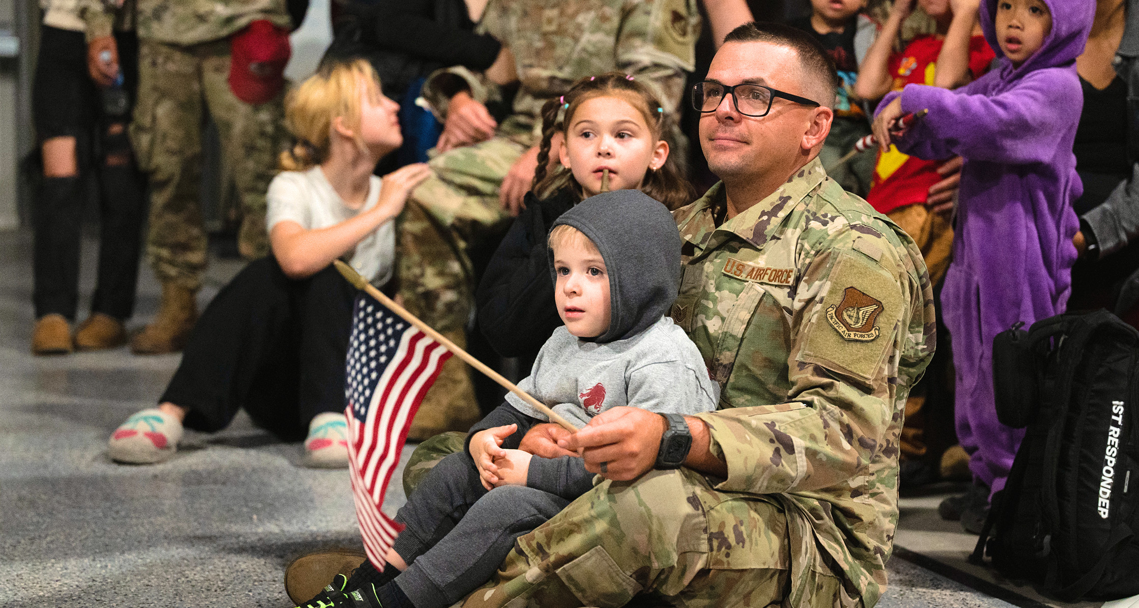 An airman sits with his children at a redeployment commencement.