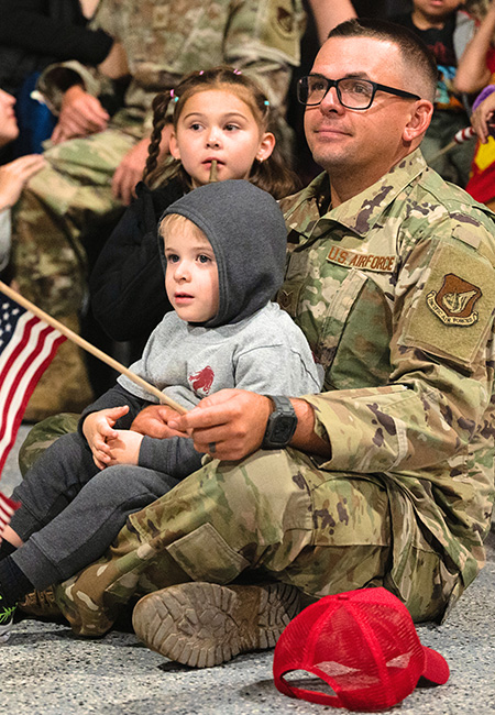 An airman sits with his children at a redeployment commencement.