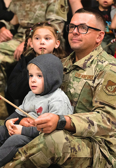 An airman sits with his children at a redeployment commencement.