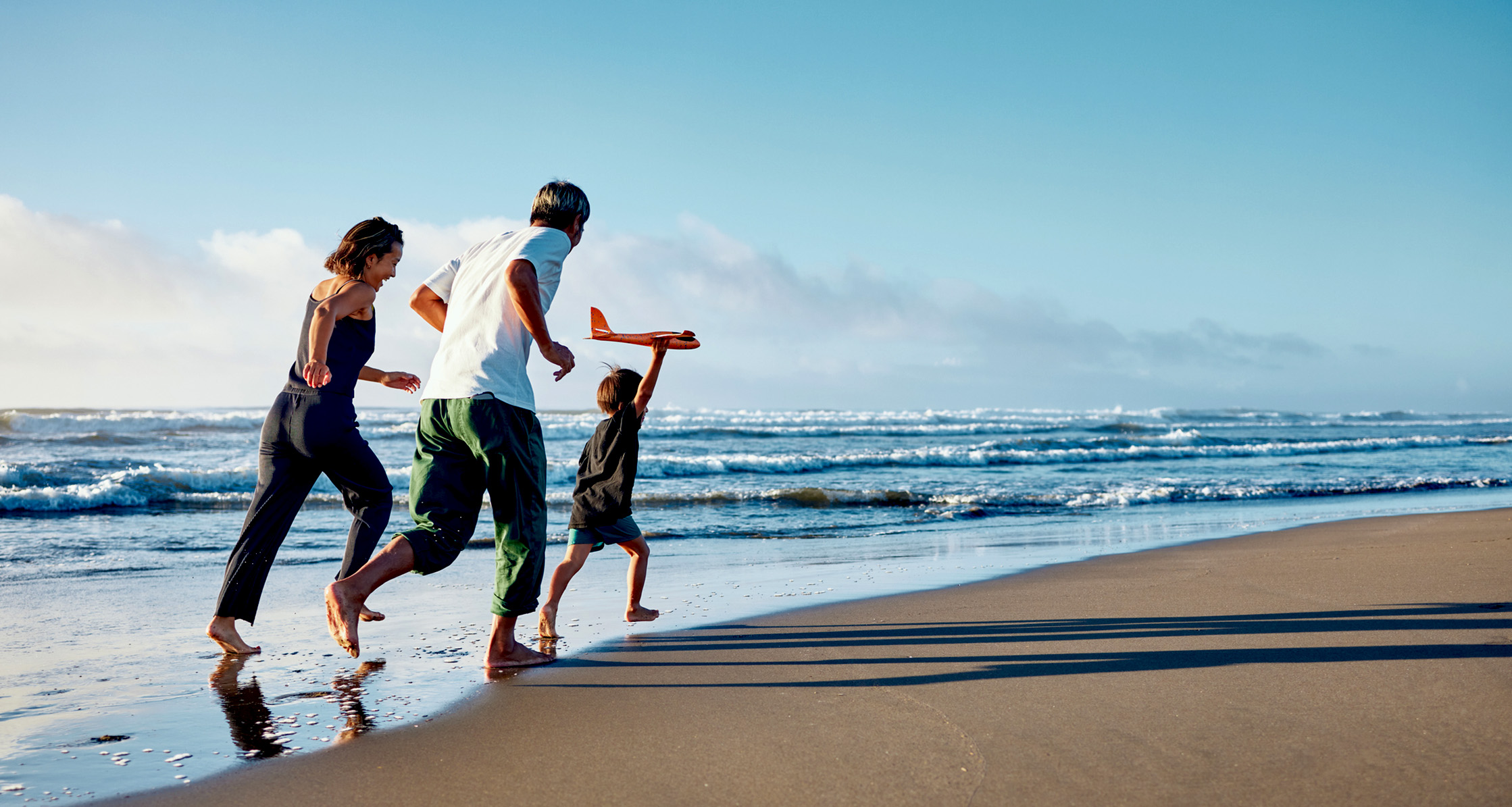A military family stays active at the beach, running after a boy with an airplane.