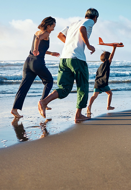 A military family stays active at the beach, running after a boy with an airplane.