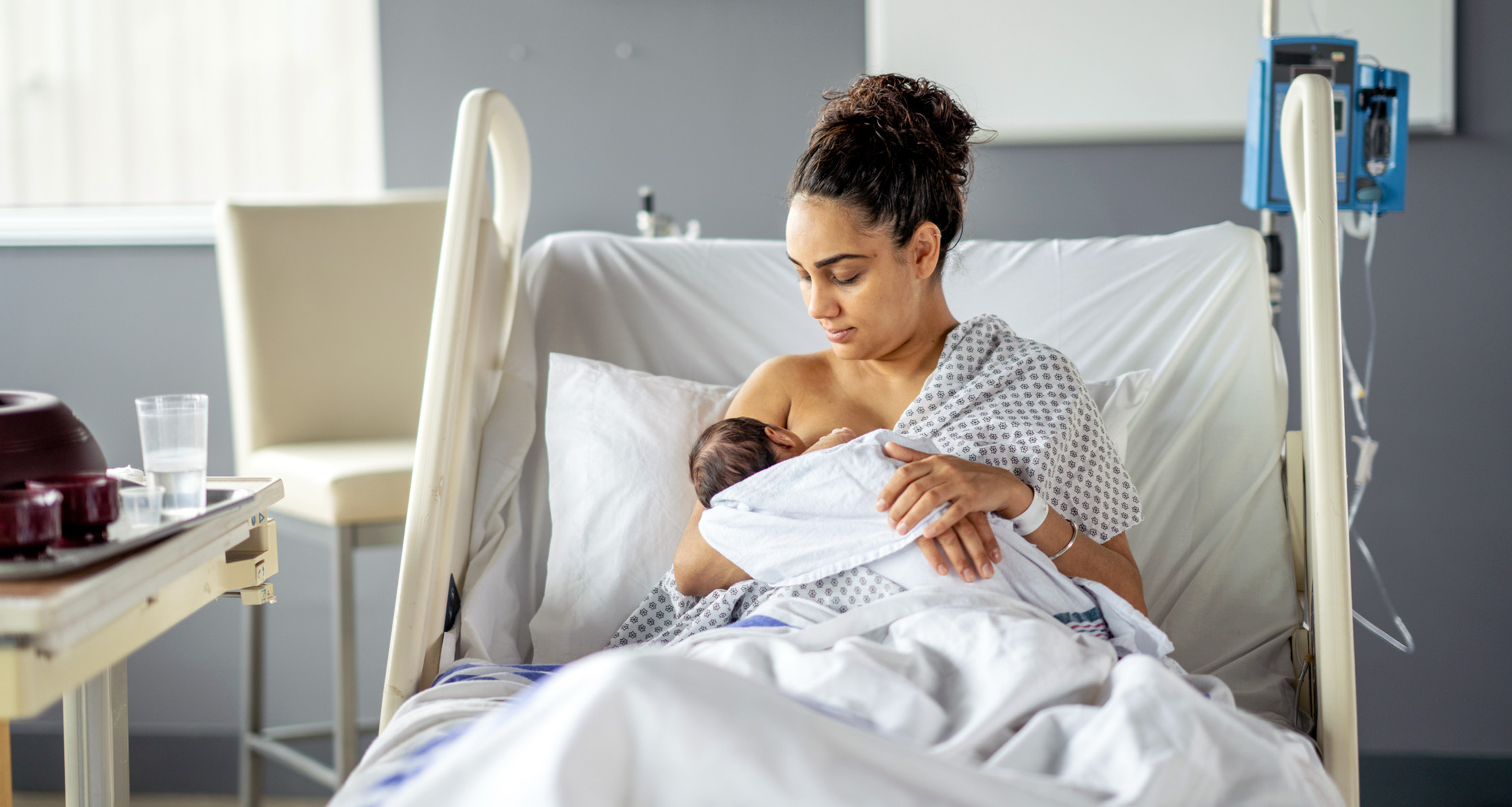 A new mother is breastfeeding her newborn in the hospital room.