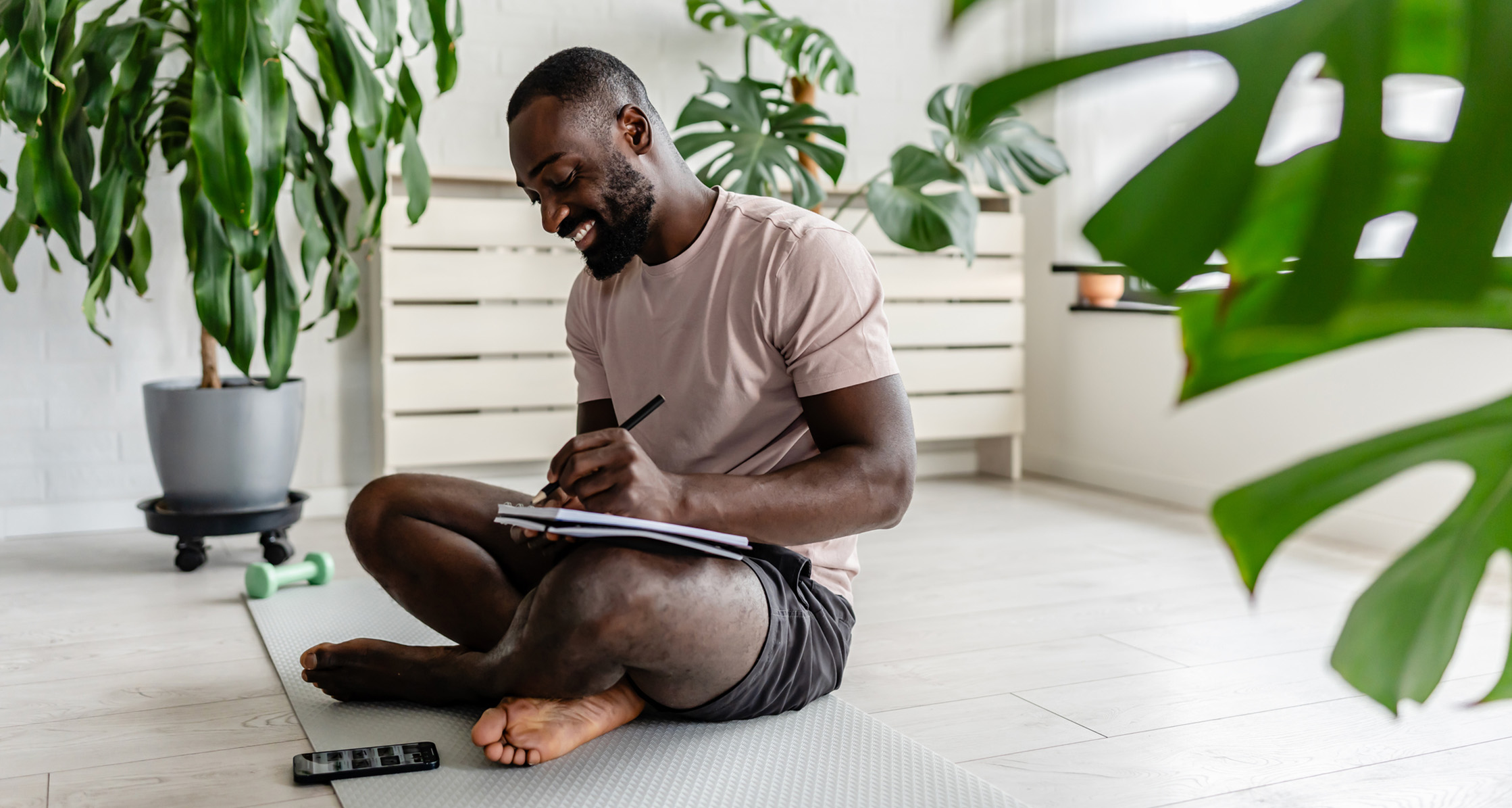 A man sitting on a yoga mat and journaling in a notebook.