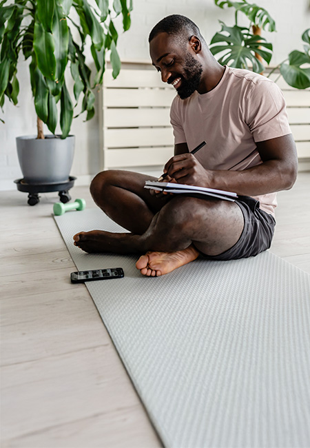 A man sitting on a yoga mat and journaling in a notebook.