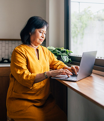 A woman sitting at a table using a computer to journal.