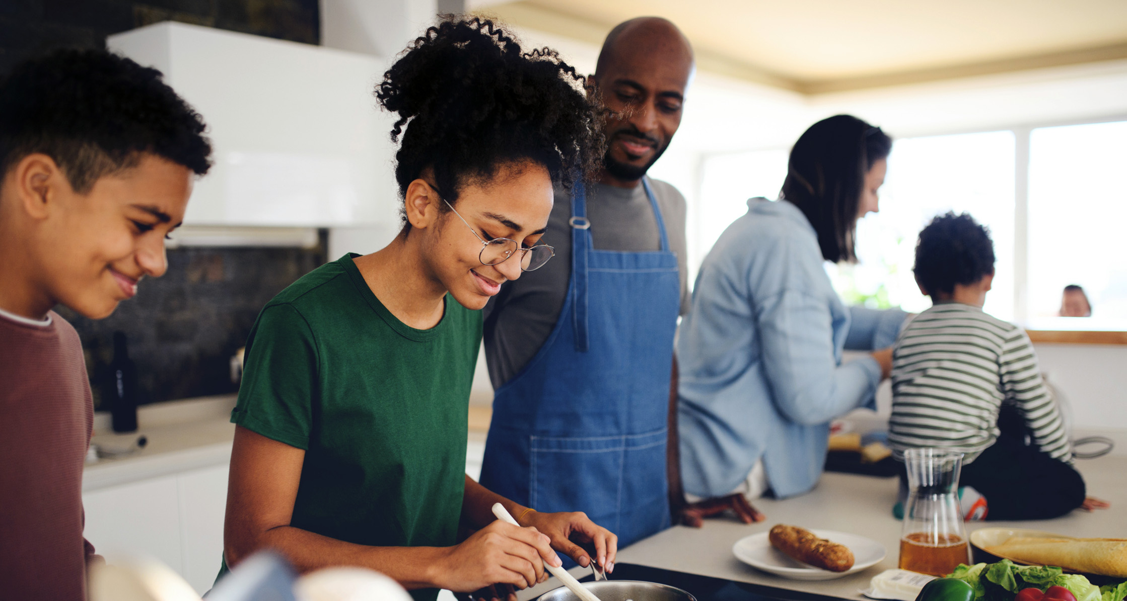 A father prepares food with his teenagers at home.