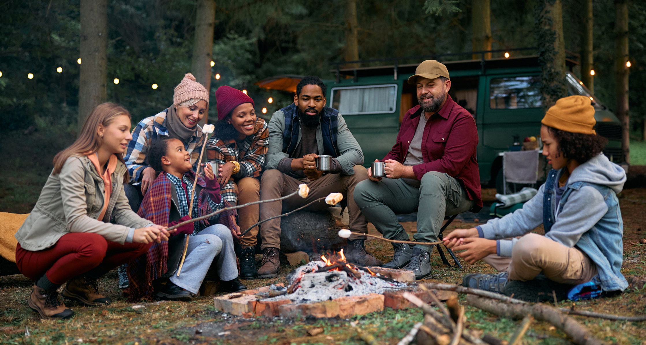 Family friends roast marshmallows over a campfire in the woods.