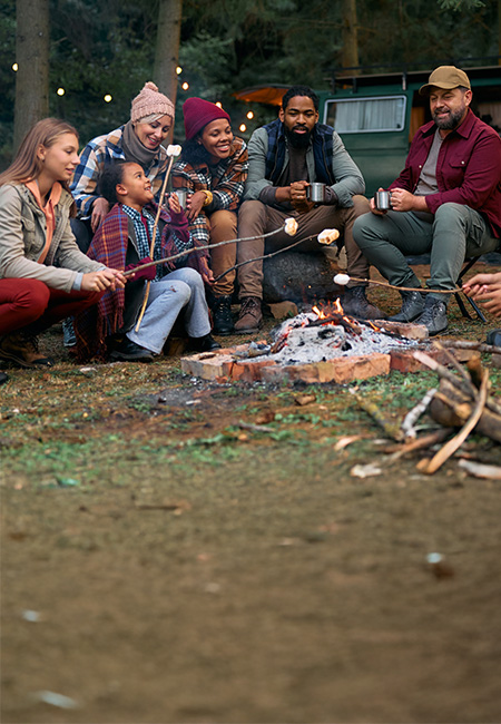 Family friends roast marshmallows over a campfire in the woods.