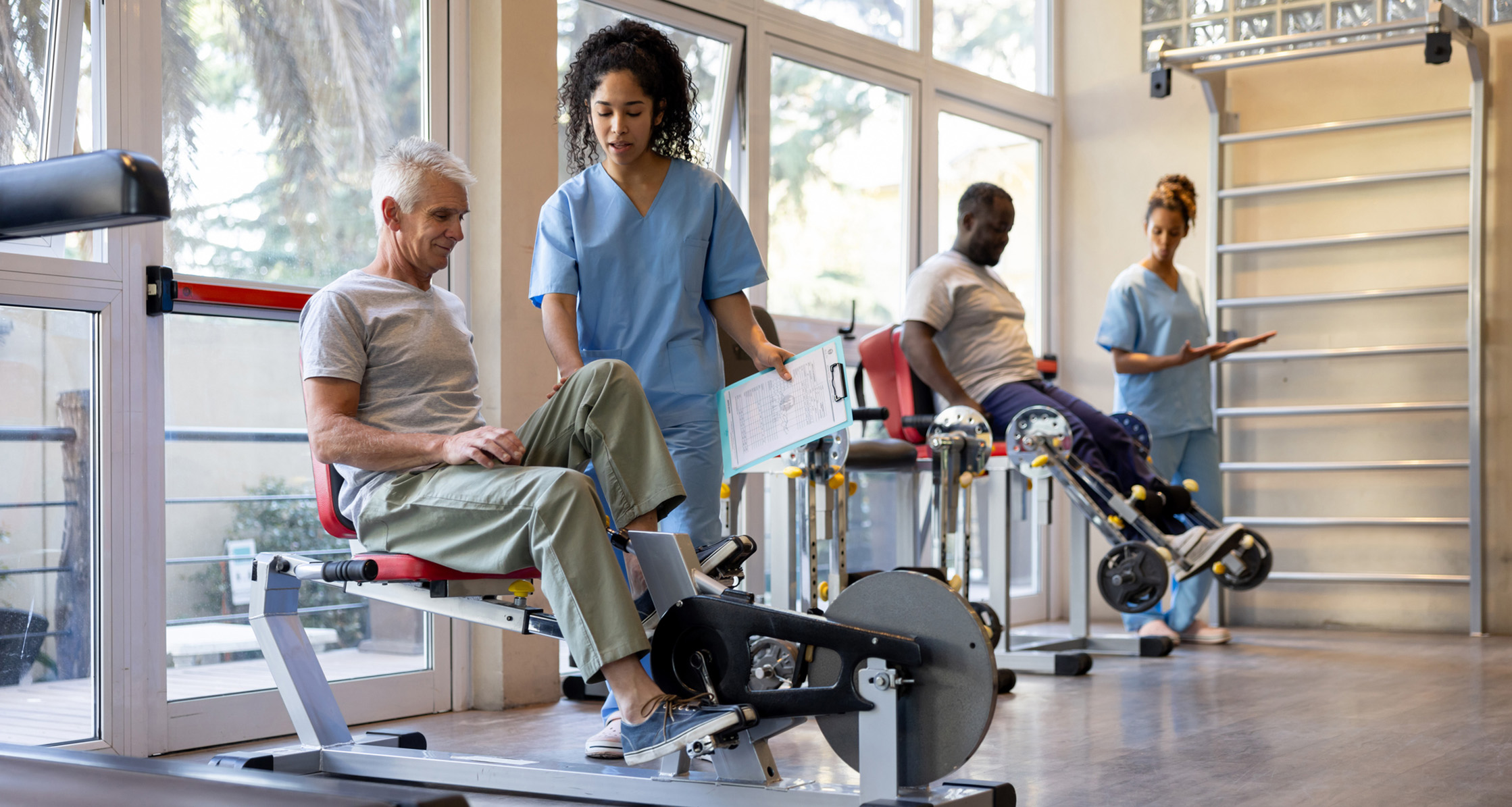 Occupational therapists assist patients using exercise equipment in a rehab clinic.