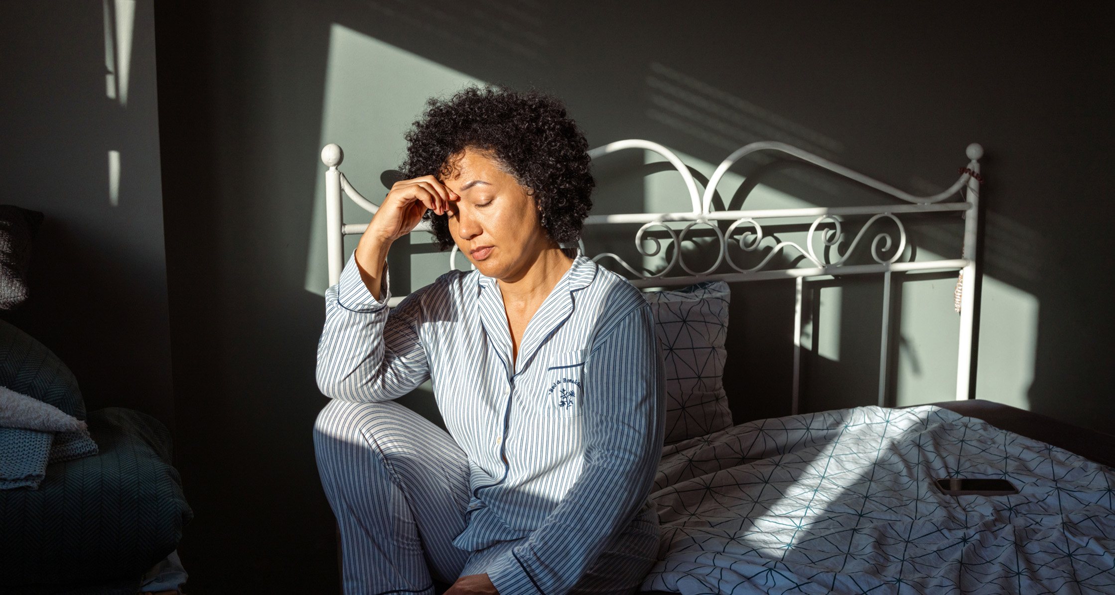 A woman in pajamas, feeling fatigued after waking up, sitting on the bed in the morning.