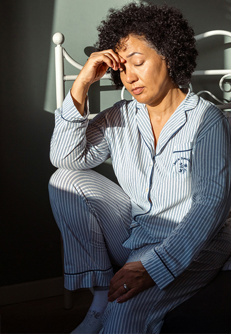 A woman in pajamas, feeling fatigued after waking up, sitting on the bed in the morning.
