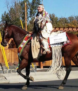 Adrienne Farrow riding her horse while dressed in Umatilla native attire.