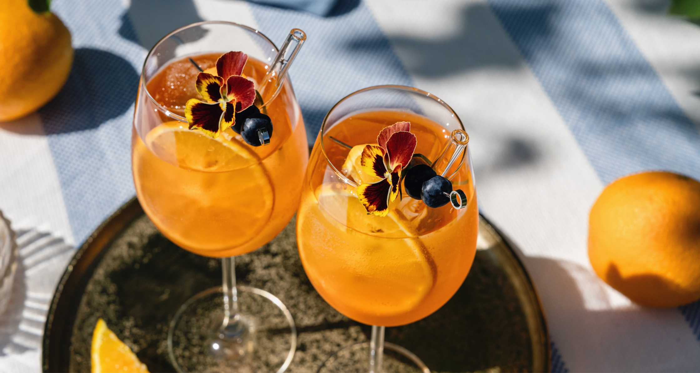 Two mocktail glasses of spritz with orange and flower garnish.