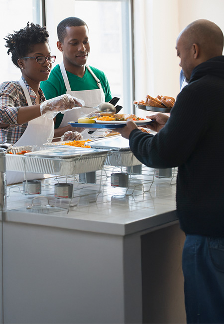 Volunteers serving hot meals to homeless Veterans in a cafeteria.